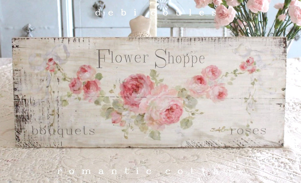 Off white background with lots of distressing. A swag of pink roses with leaves and buds create a wonderful backdrop for the slogan "Flower Shoppe" Perfect for your shabby chic, or french chic