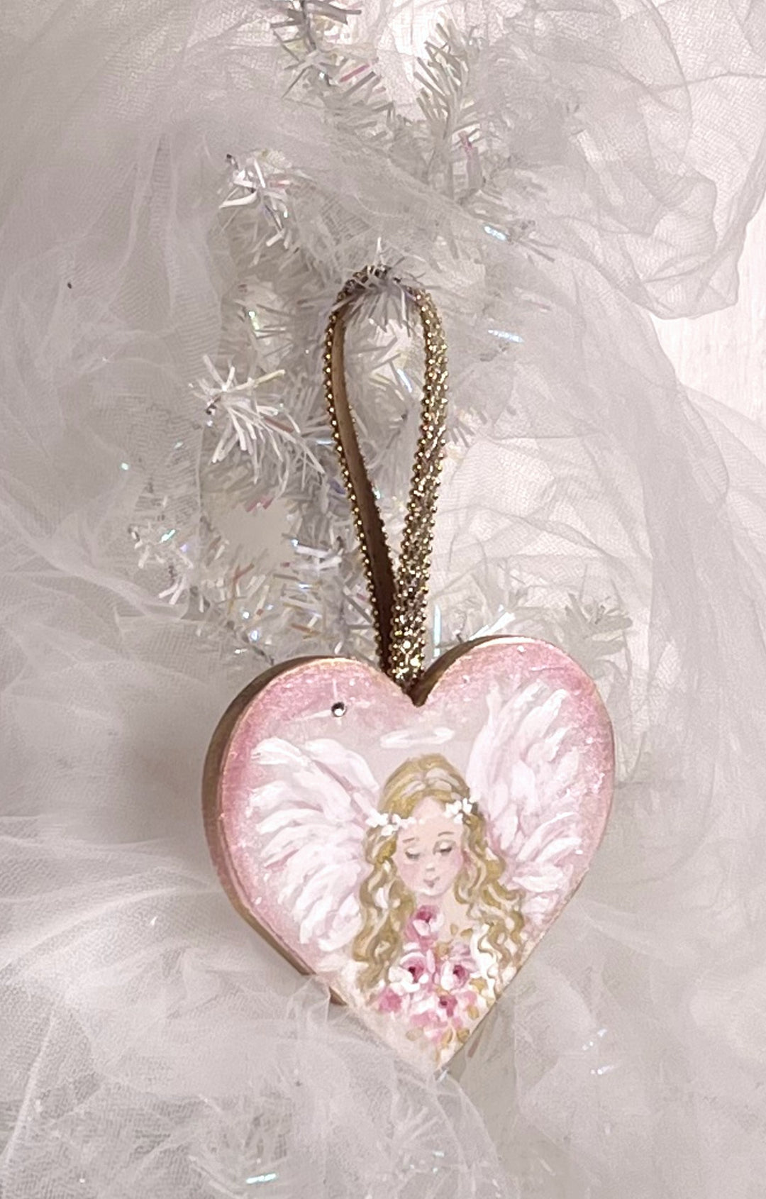 Heart-shaped angel ornament with pink and gold details on a white fluffy background