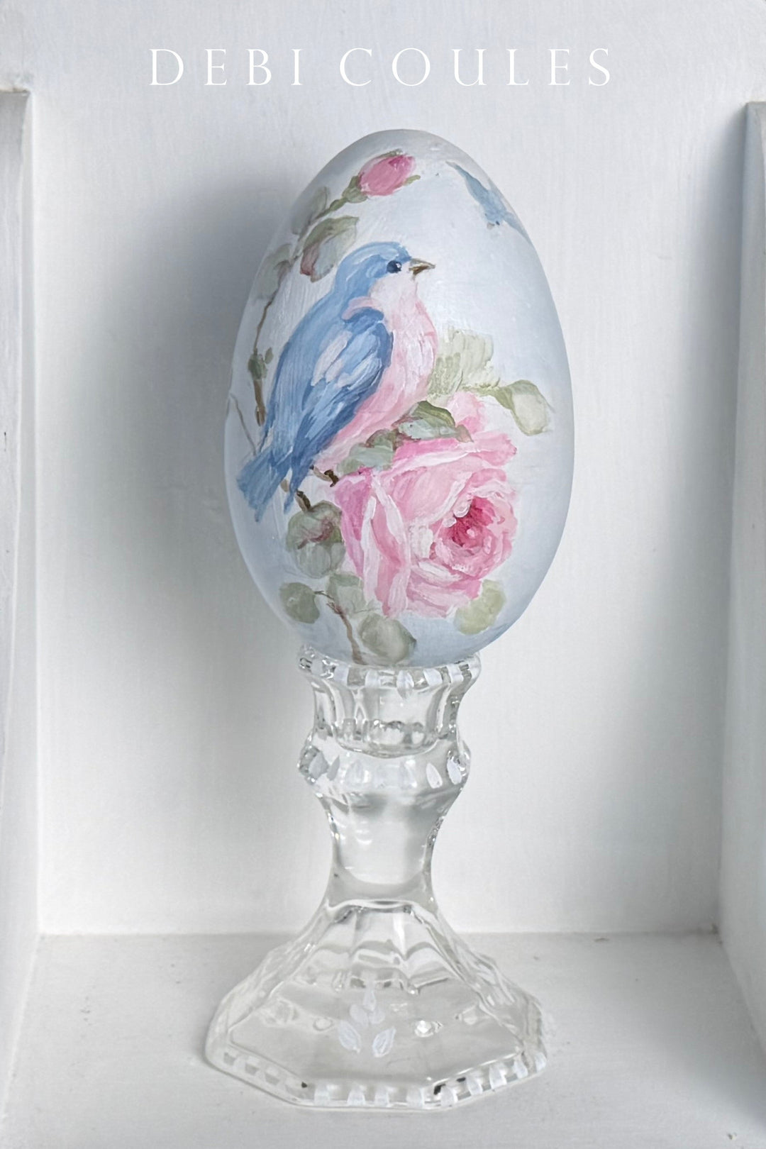 Decorative egg with floral and bird design on a stand against a white background