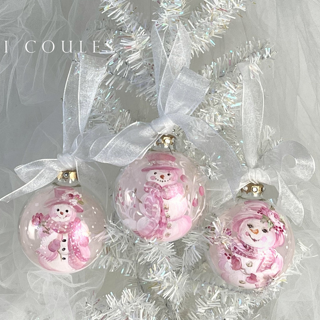 Set of three pink snowman-themed Christmas ornaments on a white ribbon against a white tinsel background.