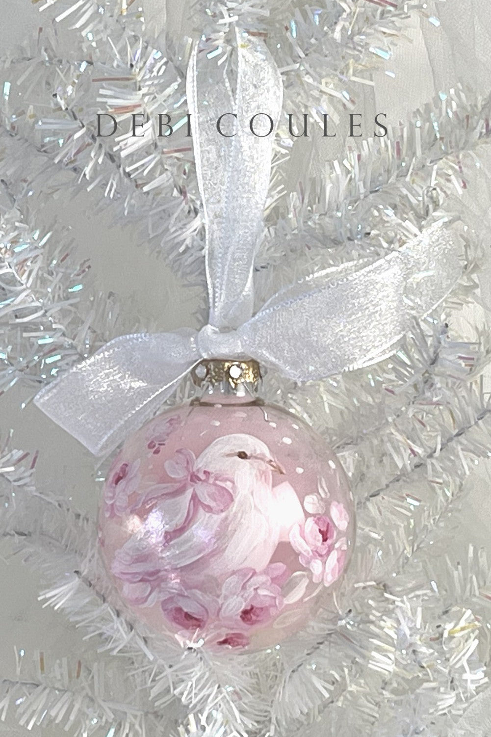 Decorative glass Christmas ornament with a dove with a pink bow hanging in white tinsel
