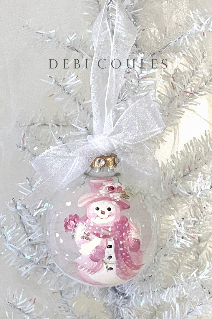 Christmas ornament with a pink snowman design on a white background, featuring the brand 'Debi Coules'.