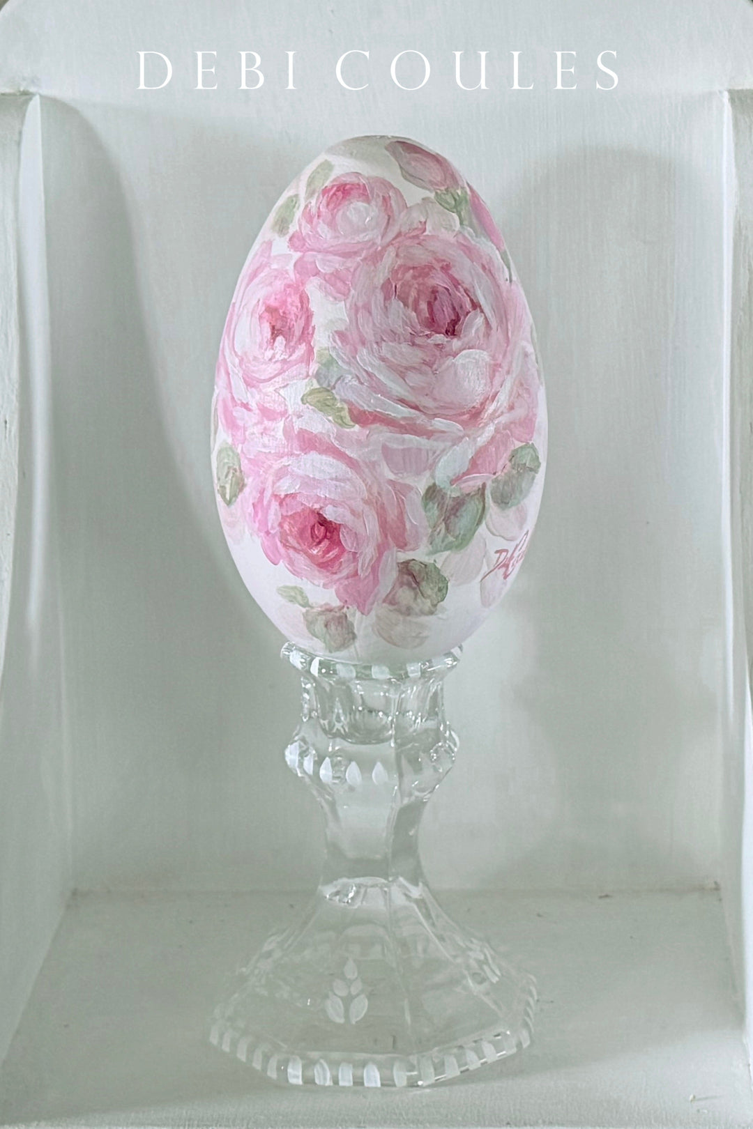 Decorative egg with floral design on a glass hand painted stand against a white background be Debi Coules