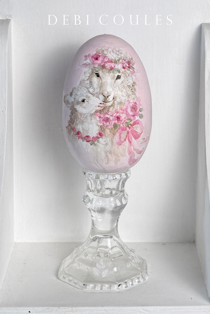 Decorative egg with sheep and floral design on pink with hand painted glass stand on a stand by artist  'Debi Coules'.