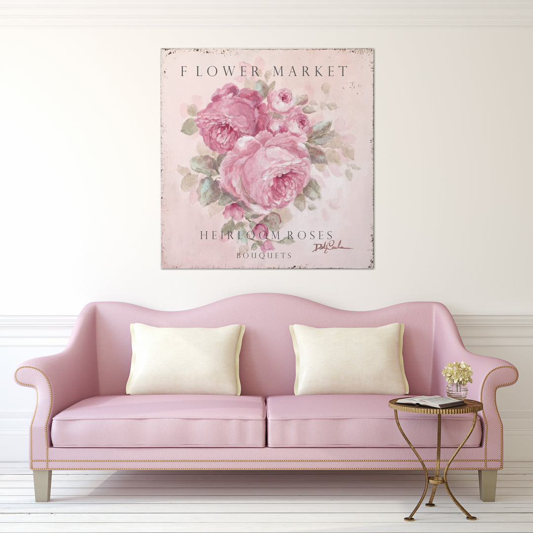 A large cottage sign of pink heirloom roses hangs above a vintage pink couch.