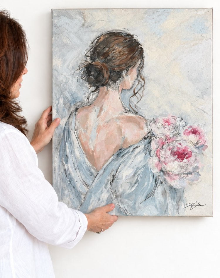 Artist Debi Coules holding up her new original painting of a woman holding a bouquet of pink peonies