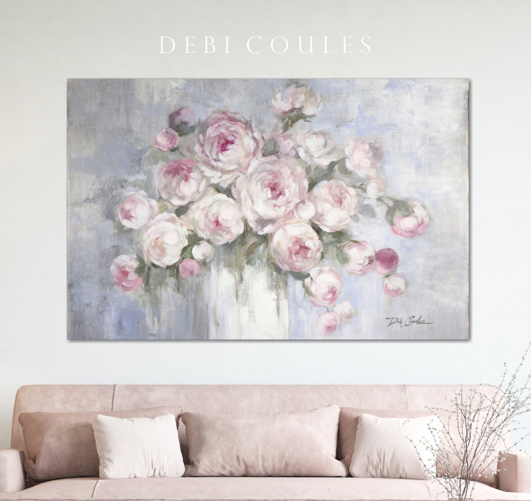 A shabby chic canvas print of pink peonies hangs above a plus, tan sofa