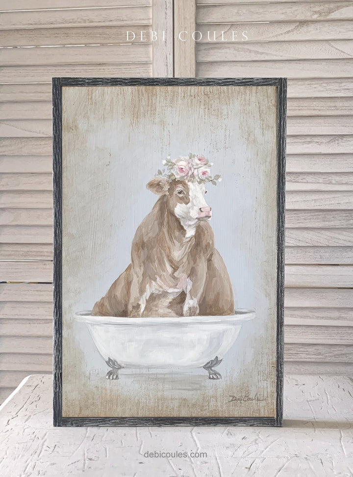 A Beautiful Tan Cow lounging in a vintage bathtub is sure to make you smile. She has a floral crown hightlighted with pink roses. , various shades of pink, off pink, mauve, whites on a blue grey background. Lots of shabby chic, modern farmhouse, and cottage warmth. Fabulous art by Debi Coules
