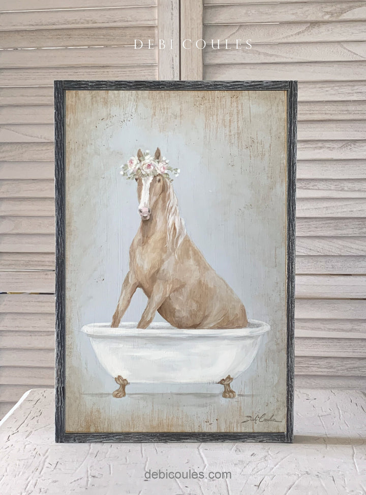 Brown horse with a crown of eden roses, pink and white around it's head. Background is a blueish green. He is  sitting in a white antique bathtub. Print on wood by Debi Coules