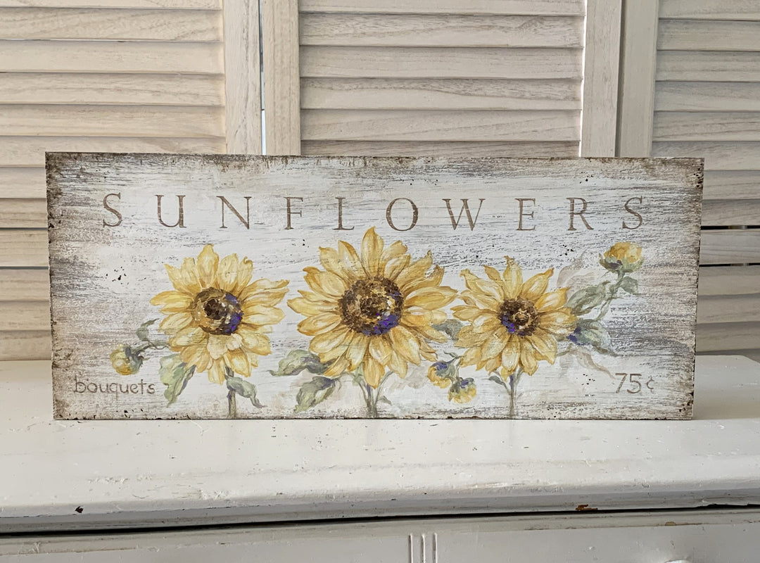 A vintage shabby off white sign caries the message...Sunflowers 75 cents. Three brilliant yellow sunflowers give the message substance.