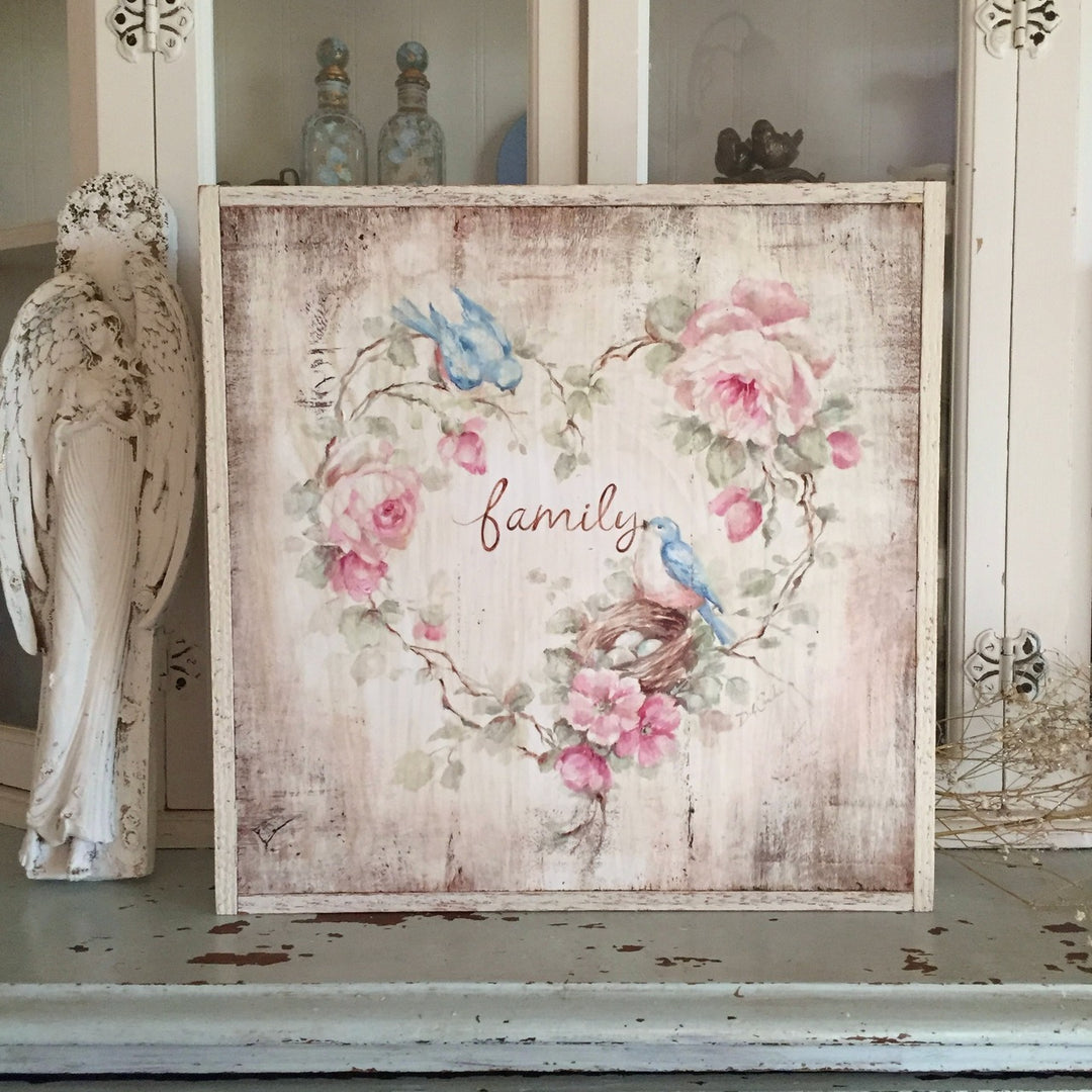 Wood framed print on wood. Vines of roses in the shape of a heart surround the word, "Family". Amoung the vines is a nest full of blue eggs and there are two bluebirdswatching over carefully.