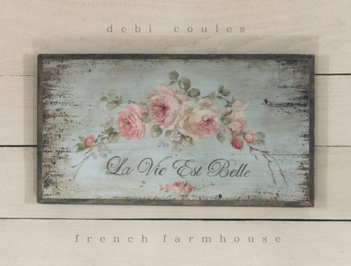 Pink roses trailing across a teal background stating, la vie est belle! Life is beautiful! in French, This Shabby chic wood giclee print is framed in 1-1.2" Barnwood by Debi Coules, Pinkish white roses swag, warm colors, worn distressed look, solid wood, sawtooth hanger